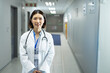 © wavebreak3 - Asian woman standing and smiling in hospital hallway, wearing lab coat, stethoscope and ID badge