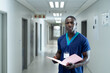 © wavebreak3 - African American male nurse reviewing pink folder in hospital corridor wearing ID badge, copy space