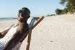 © wavebreak3 - African American man reclining in deck chair on beach, wearing striped top, sunglasses, copy space