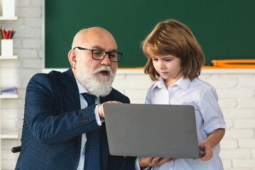 Fototapete - Senior teacher and school child. Mature teacher helps school child learn. School teacher and child in classroom. Teacher in school on lesson teach child on laptop.