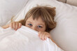 © New Africa - Bedtime. Cute little girl covering mouth with blanket in bed