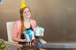 © WavebreakMediaMicro - Woman sitting at home office desk holding wrapped gifts with chocolate cake and laptop, copy space