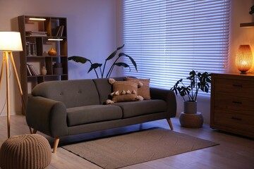 Poster - stylish living room with comfortable sofa and wooden shelving unit in evening. interior design