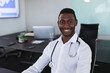 © Wavebreak Media - Young African American doctor sitting at table in office, smiling with stethoscope and laptop