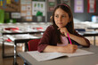 © Wavebreak Media - Elementary school girl writing in notebook at gray classroom desk in red chair with pink pencil