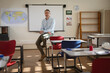 © Wavebreak Media - Male teacher sitting casually on desk in school classroom, with whiteboard and world map poster