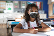 © Wavebreak Media - 10-year-old girl sitting at desk in classroom writing in notebook with pencil wearing face mask