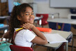 © Wavebreak Media - bi-racial schoolgirl sitting at desk smiling in classroom, holding pencil near orange pencil box