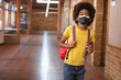 © Wavebreak Media - Boy standing in school hallway, with red backpack displaying purple straps and black face mask