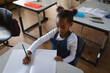 © Wavebreak Media - African American girl child writing in open notebook at school desk in classroom, with green pencil