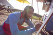 © Wavebreak Media - Young African American man kneeling writing on chalkboard menu by food trailer, wearing red apron