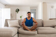 © Wavebreak Media - Man meditating cross?legged on sectional sofa in living room, with potted plant and clock