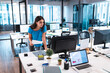 © Wavebreak Media - Young adult woman leaning over white desk in modern office reviewing paper at black monitor