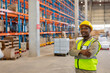 © Wavebreak Media - African American warehouse worker crossing arms in warehouse, wearing helmet and vest, copy space