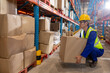 © Wavebreak Media - Mature Asian man crouching in warehouse aisle handling cardboard box, with shelving, copy space