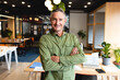 © Wavebreak Media - Mature adult man posing with arms crossed in modern open-plan office, showing laptop, potted plants