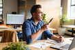 © Wavebreak Media - Young man speaking into smartphone at modern office desk, with laptop, papers and glass of water