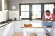 © Wavebreak Media - African American teenage boy sitting on island in modern kitchen, using smartphone, copy space