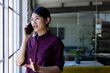 © Wavebreak Media - Young Asian Chinese woman talking on smartphone while gesturing by multi-pane window in office