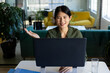 © Wavebreak Media - Asian woman sitting at desk in office lounge, gesturing and smiling during video calling on monitor