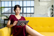 © Wavebreak Media - Young Asian woman sitting on bright yellow sofa tapping tablet in modern lounge with mountain view