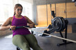 © Wavebreak Media - Woman using rowing machine in gym, showcasing focused workout and natural sunlight