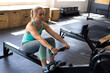 © Wavebreak Media - Mid-adult woman rowing on machine in gym, with plyo boxes and digital monitor, copy space