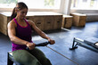 © Wavebreak Media - Young adult woman pulling handlebar on rowing machine in gym, with plyometric boxes, copy space