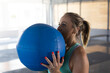 © Wavebreak Media - Woman lifting large blue medicine ball toward face in fitness studio, showcasing strength training