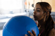 © Wavebreak Media - Woman holding large blue medicine ball close to face in bright indoor gym with weight benches
