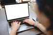 © Thaspol - Woman typing on laptop with blank screen at a wooden table in modern indoor setting, suitable for UI mockup or workspace concept.
