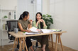 © Johnstocker - Portrait of Two female colleagues are sitting together at desk, reviewing documents and discussing work in the office.