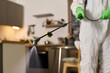 © pressmaster - Close-up of worker in suit spraying in the room and disinfecting apartment from insects