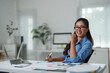 © crizzystudio - Smiling businesswoman sitting at office desk with laptop and analyzing charts and graphs, showing successful financial results and business growth