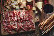 © BONI - Tabla de embutidos con jamón curado, queso, pan y copa de vino tinto sobre mesa de madera rústica en luz cálida.