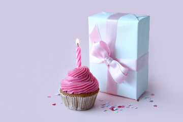 Wall Mural - tasty cupcake with birthday candle and gift box on lilac background
