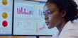 © Georgy - A woman of mixed race, wearing a lab coat and glasses, works in the medical profession, carefully looking at a monitor with health data in a hospital environment illuminated by natural light
