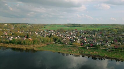 Wall Mural - drone footage showing a lush green countryside merging into a reflective river near a compact latvia