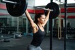 © alisaaa - Female athlete lifting heavy barbell overhead in a gym. Side view of a woman performing weightlifting exercise in a fitness studio.