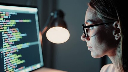 Aufkleber - Female programmer wearing glasses typing code intently at desk, illuminated by warm lamp glow while focusing on complex software development project in dimly lit home workspace