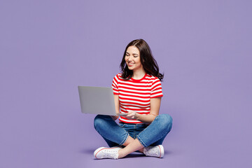 Full body young happy IT woman she wear red striped t-shirt casual clothes sit hold use work on laptop pc computer isolated on plain pastel light purple background studio portrait. Lifestyle concept.