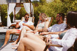 © djile - Group of friends enjoying summer vacation, relaxing in deck chairs by the pool, chatting and having fun