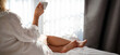 © nickolya - Young woman in a bathrobe sitting on the bed and drinking coffee.