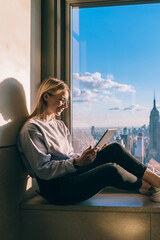 Wall Mural - Happy female freelancer checking information while watching streams video via modern touch pad with 4g, smiling hipster tourist reading text publication with trip advisor for exploring New York