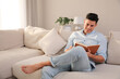 © New Africa - Man reading book on sofa in living room