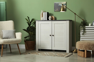 Aufkleber - Cabinet with different decor, lamp, pouf and armchair near green wall indoors. Interior design