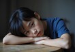 © TanvirAhamed - Thoughtful Young Asian Boy with Melancholic Expression Resting on Table,Generative AI