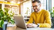 © sun - Bright cheerful man wea glasses and a yellow shirt working on a laptop in a modern cozy cafe with large and lush green plants for a relaxed work environment