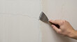 © Vasiliy - Hand using metal putty knife to repair wall crack. Close-up of filling technique with spackling compound. Home maintenance and drywall repair solutions