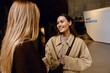 © Drobot Dean - Two young women engage in friendly conversation indoors near a modern exhibit marked 'Base Antarctica,' smiling warmly. A concept of connection, shared curiosity, and the spirit of exploration.